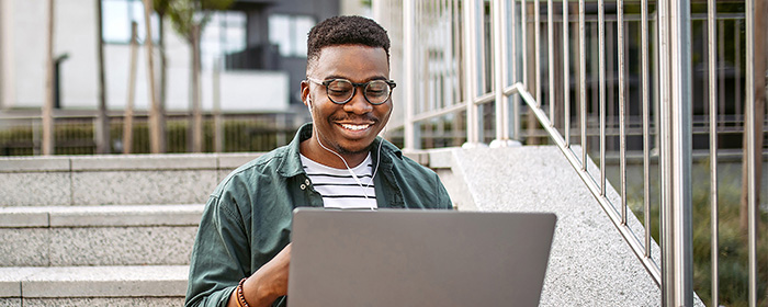 Man working on his laptop on a staircase outside.