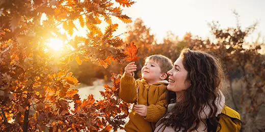 mother holding a child by a tree on autumn day